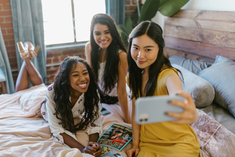 three teens girls sitting on a bed taking a picture on their phone